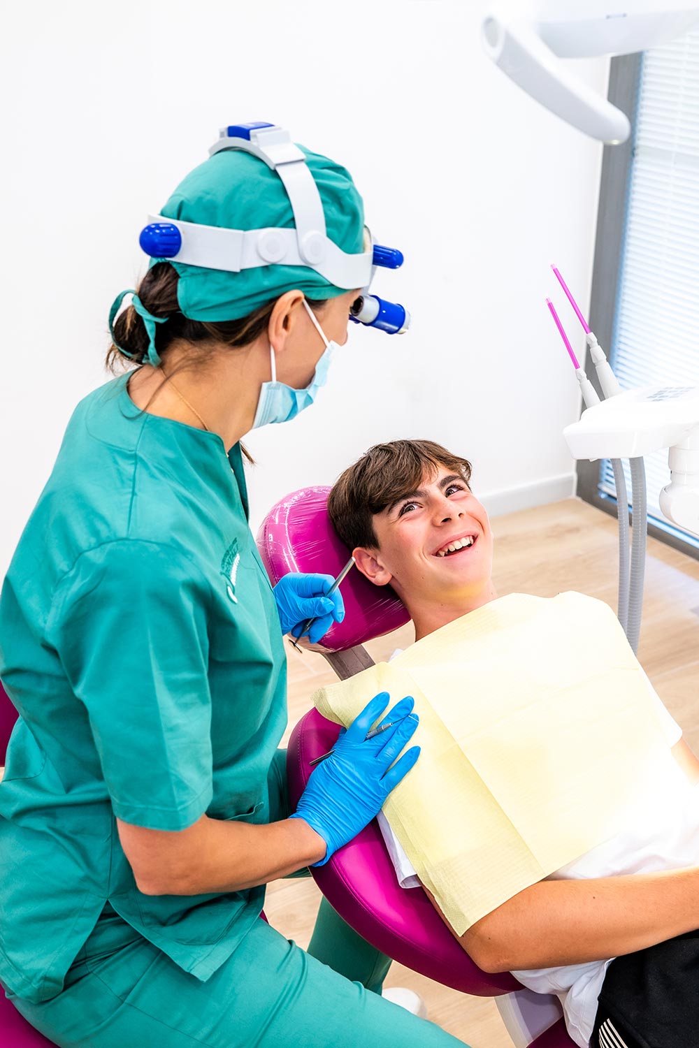 La dottoressa Daniela Demontis e la sua assistente durante una visita di controllo in studio dentistico moderno con un paziente uomo sdraiato su una poltrona fuxia